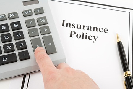 man pressing the plus button on a calculator with an insurance policy on the table